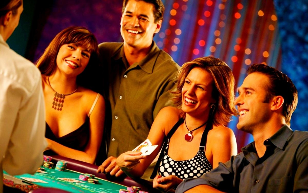 Красивые женщины в коктейльных платьях и мужчины в строгих костюмах за столом для блэкджека в компании крупье