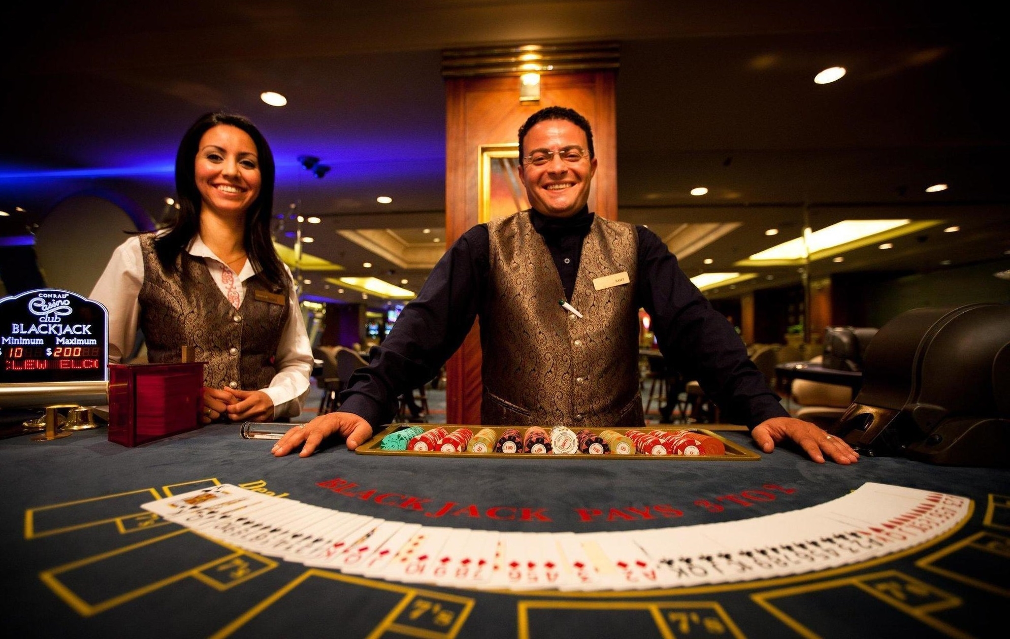 Мужчина и женщина, работающие крупье, ждут клиентов у стола для игры в блэкджек